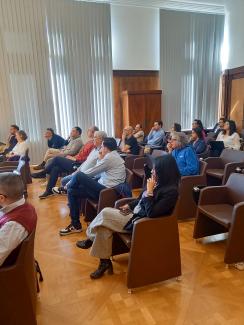 Ensemble de personnes assises qui assistent à une présentation dans une salle au décor prestigieux.