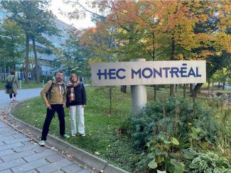Photo : deux personnes dans un environnement verdoyant devant le panneau où il est écrit HEC Montréal