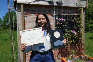 Photo de Fatima Najoui portant son prix et son attestation de réussite dans un cadre verdoyant